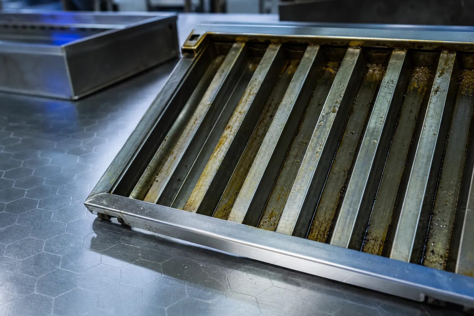 Fente de filtre de hotte aspirante métallique légèrement encrassé sur un plan de travail professionnel, prêt pour un nettoyage. Comment nettoyer filtre hotte aspirante, image illustrative.