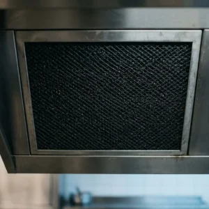 Filtre à charbon actif encastré dans une hotte, vue métallique sombre et grille de filtration visible. à quoi sert le filtre à charbon dans une hotte intégré naturellement.